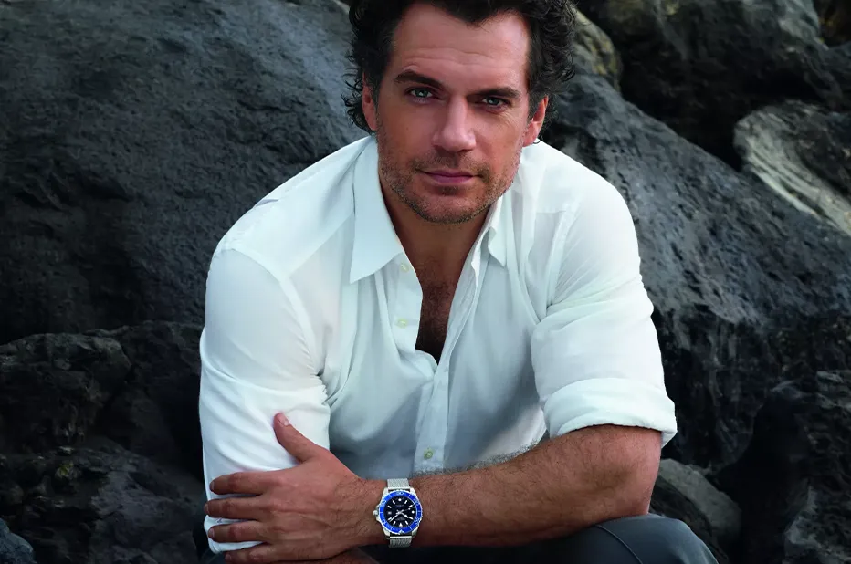 Henry Cavill na skalistym wybrzeżu z zegarkiem Longines HydroConquest z niebieską ceramiczną lunetą na nadgarstku