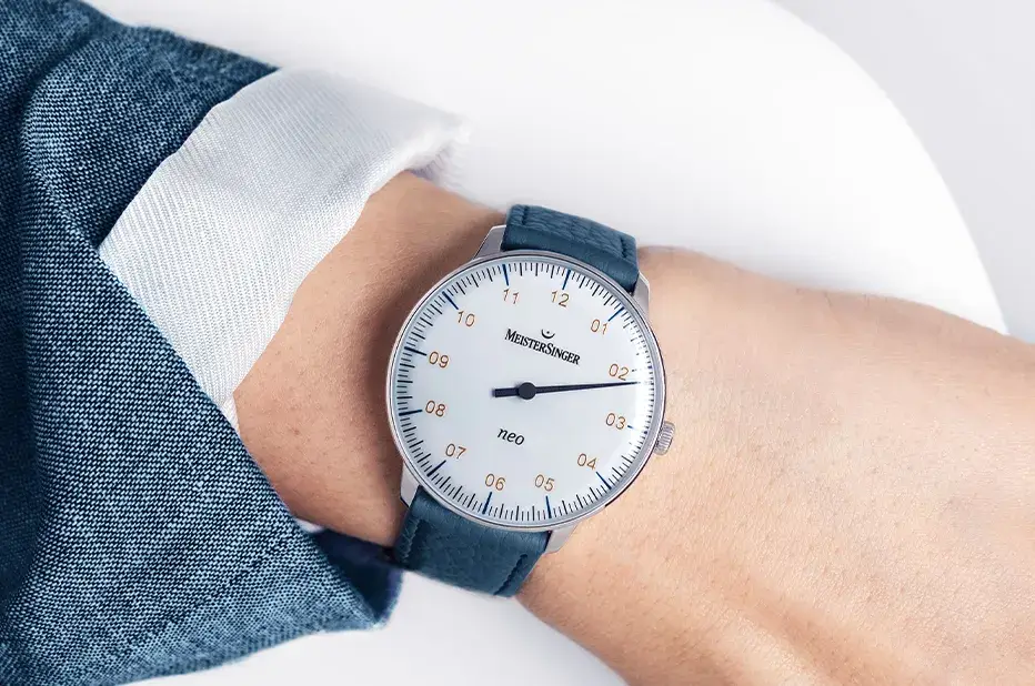 Zegarek jednowskazówkowy MeisterSinger Neo na nadgarstku – elegancki czasomierz w stylu minimalistycznym z niebieskim paskiem i białą tarczą